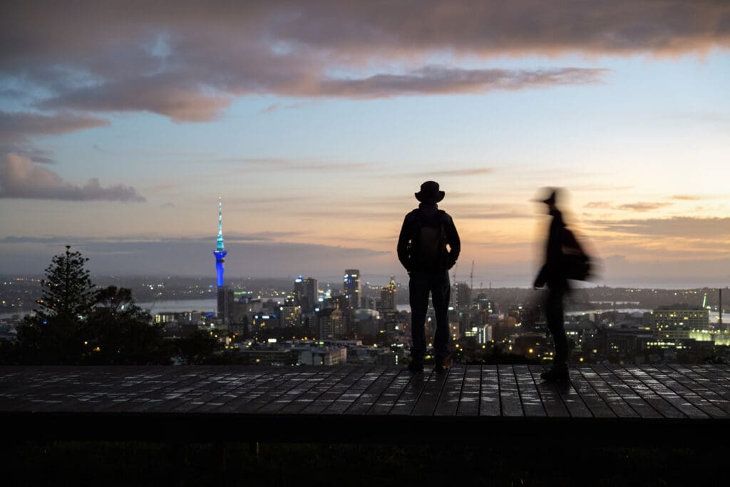 Two people standing looking over Auckland city at Sunset
